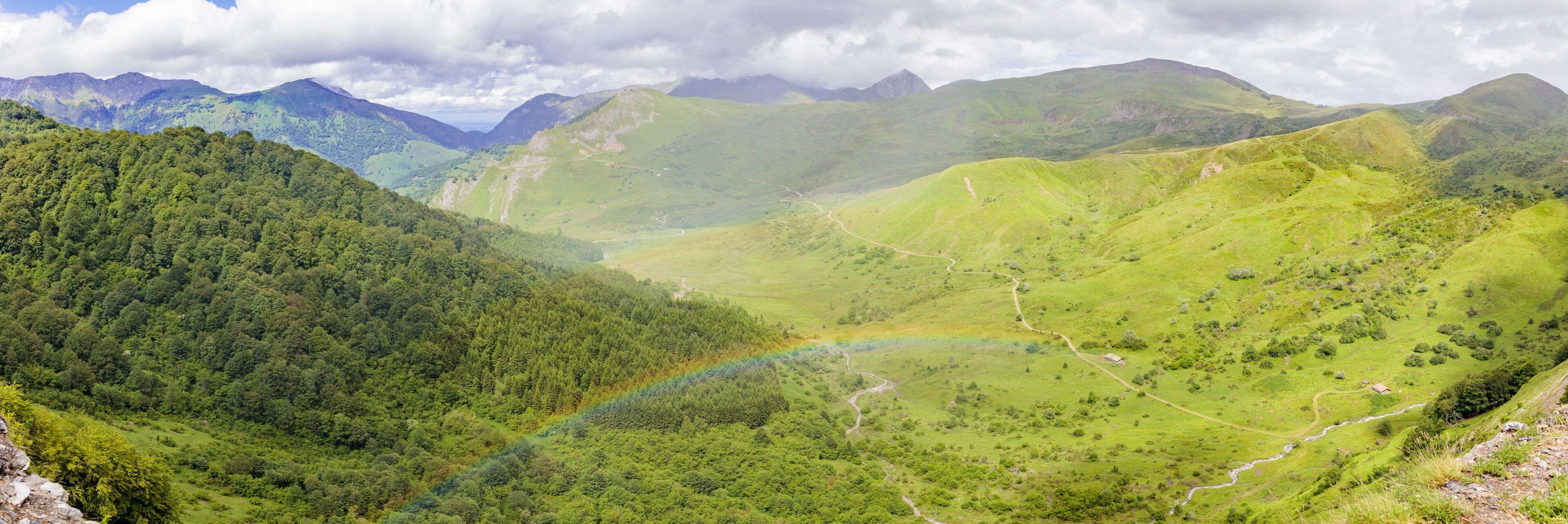 A valley with a rainbow, lush green hills, and distant mountains.