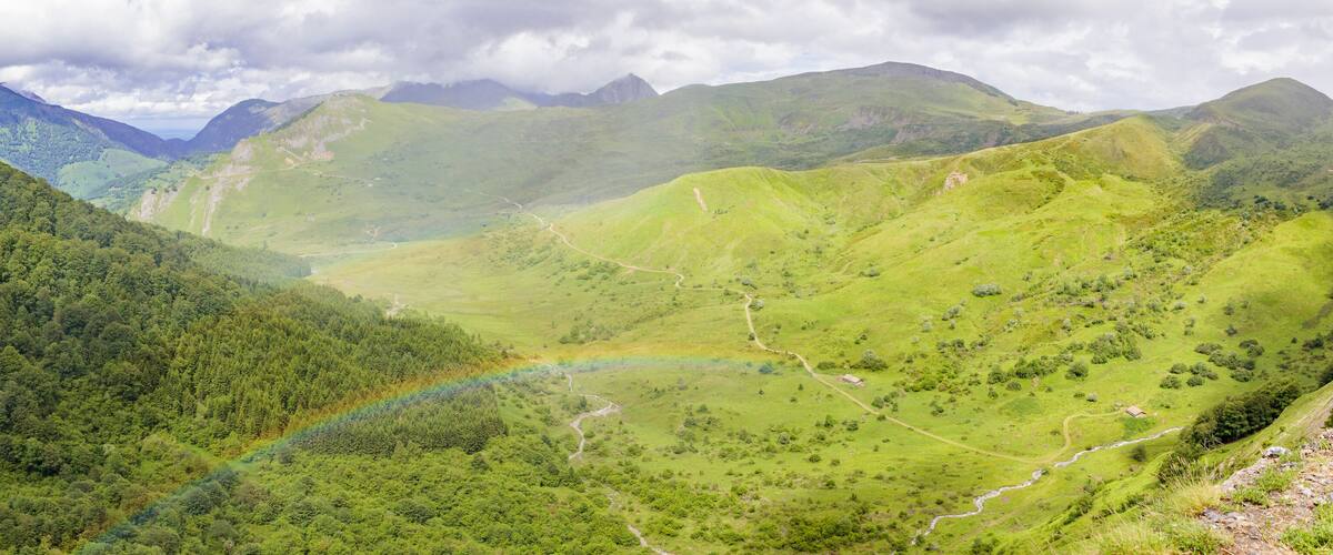 A valley with a rainbow, lush green hills, and distant mountains.