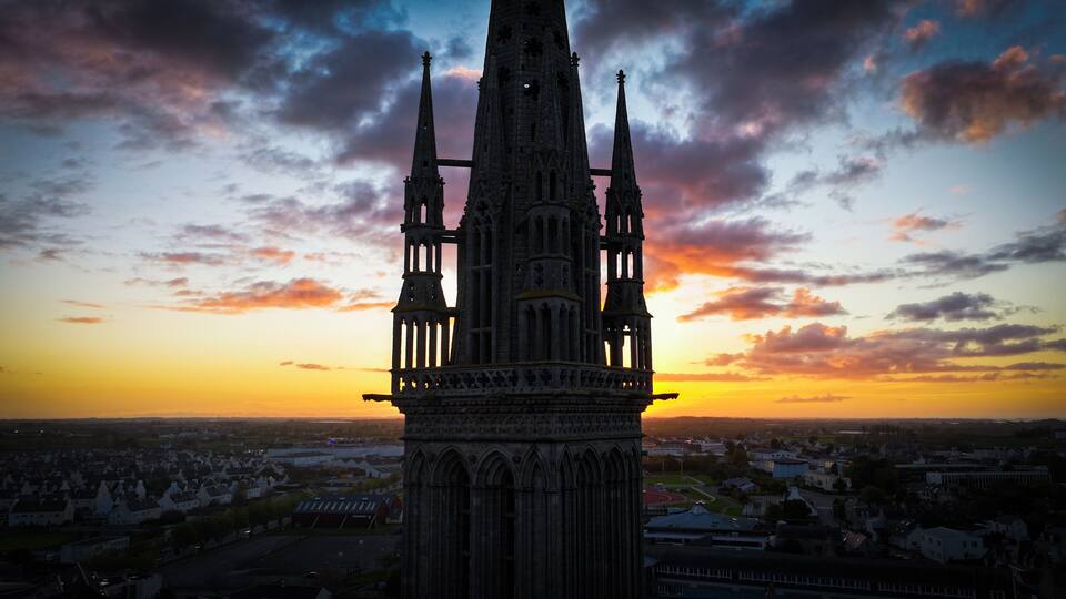A Gothic cathedral with twin spires, set against a sunset sky.