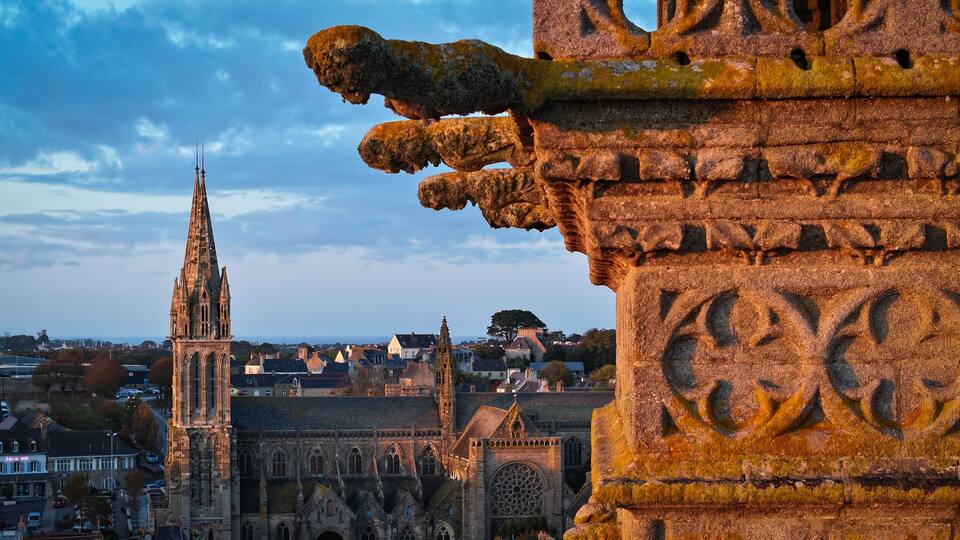 A Gothic cathedral with a tall spire, a stone gargoyle, and a medieval town in the background.