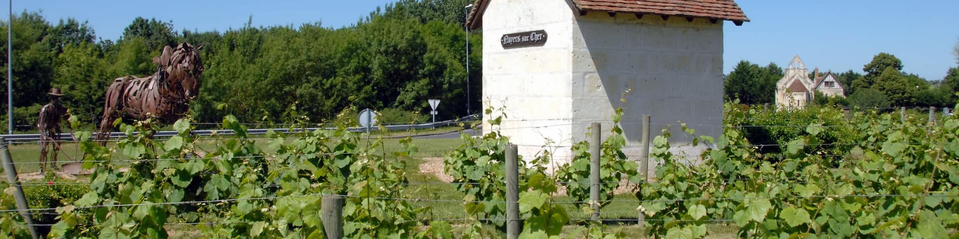 A white building with a sign reading "Pipers at Gaiety," surrounded by grapevines and a large horse statue.