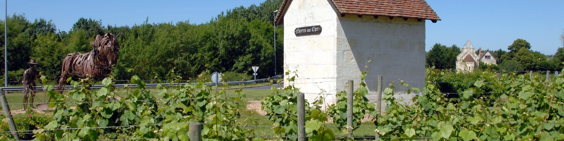 A white building with a sign reading "Pipers at Gaiety," surrounded by grapevines and a large horse statue.