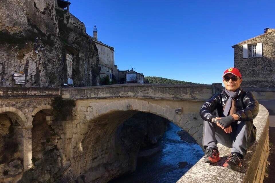 A stone bridge over a river, a historic building, and a person sitting on a ledge.