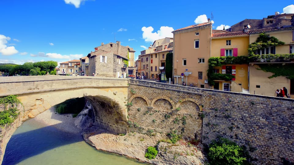 A stone bridge over a river, historic buildings, and a clear blue sky.