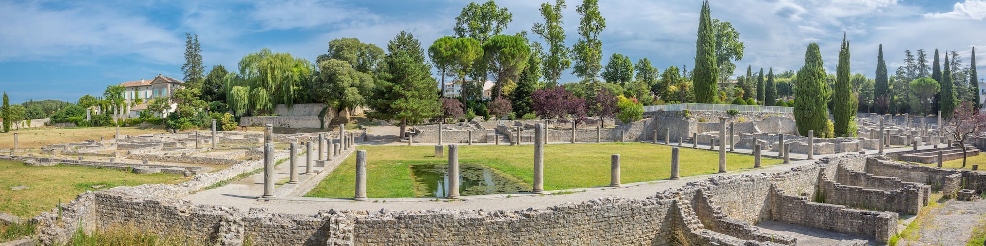 Ancient ruins with columns, a central open space, and surrounding trees.