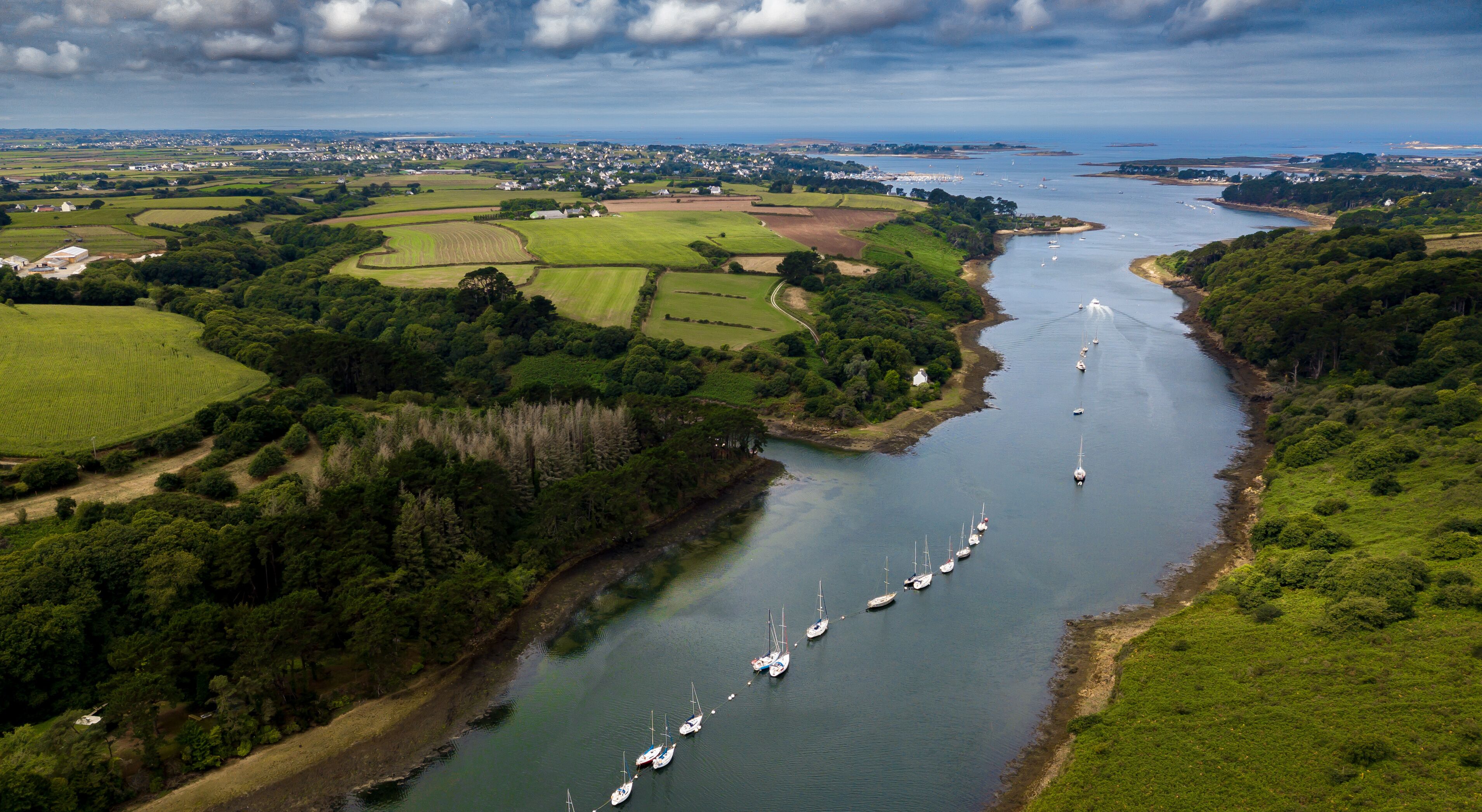 A river with sailboats, surrounded by green fields and a town in the distance.
