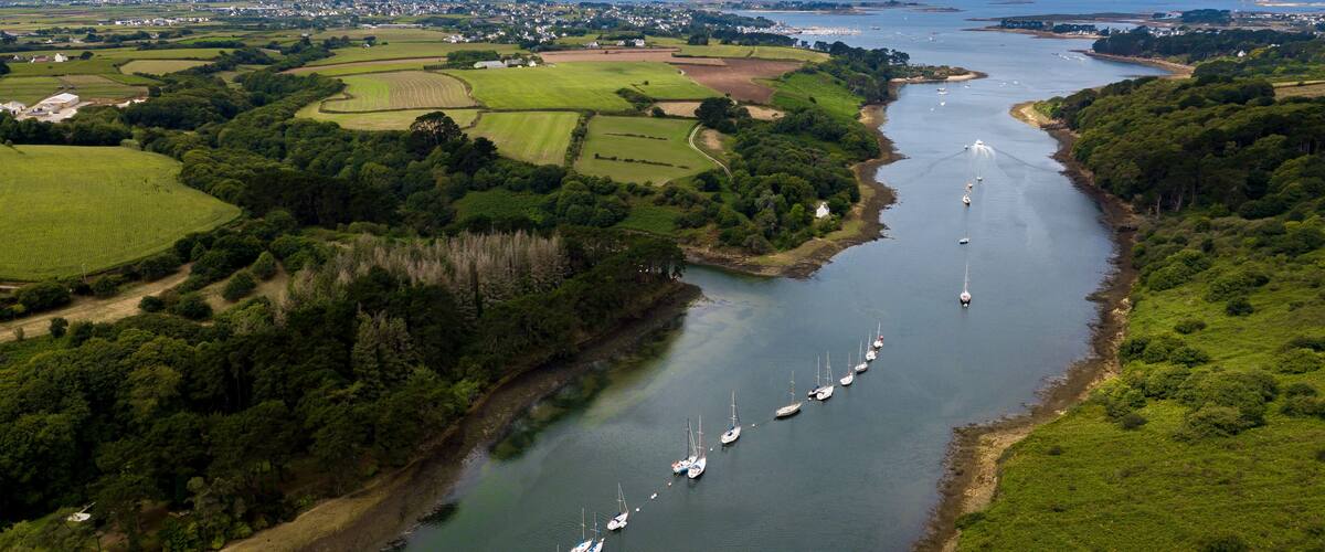 A river with sailboats, surrounded by green fields and a town in the distance.