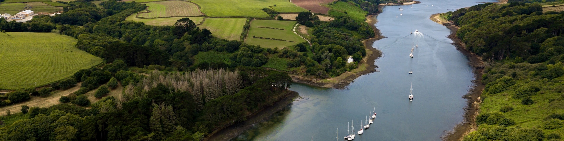 A river with sailboats, surrounded by green fields and a town in the distance.