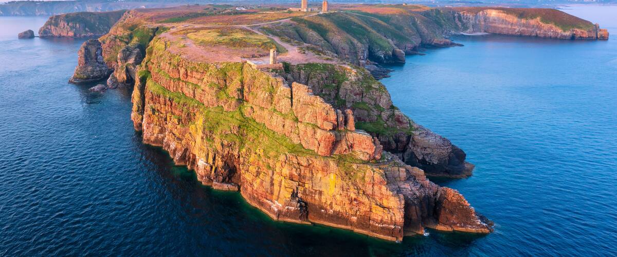 A coastal cliff with a lighthouse, rugged terrain, and a clear view of the surrounding water.