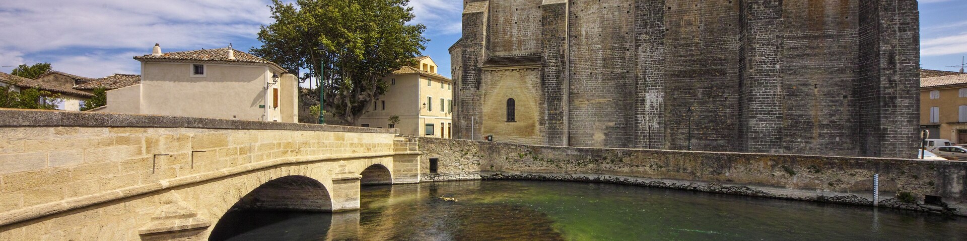 A historic stone bridge over a clear river, a large church with a bell tower, and surrounding buildings.