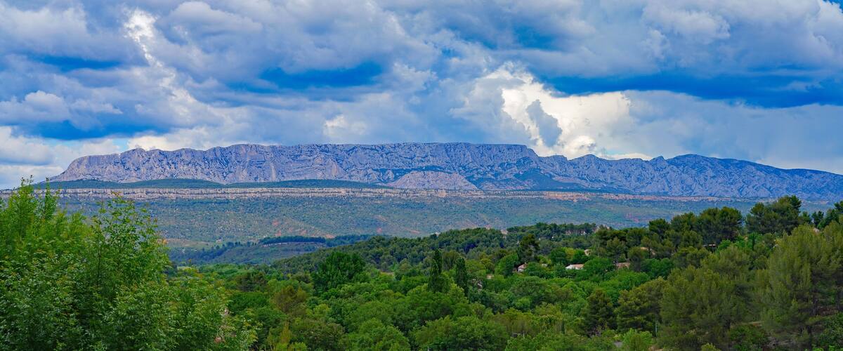 A mountainous landscape with a range of rocky peaks and a foreground of dense green trees.