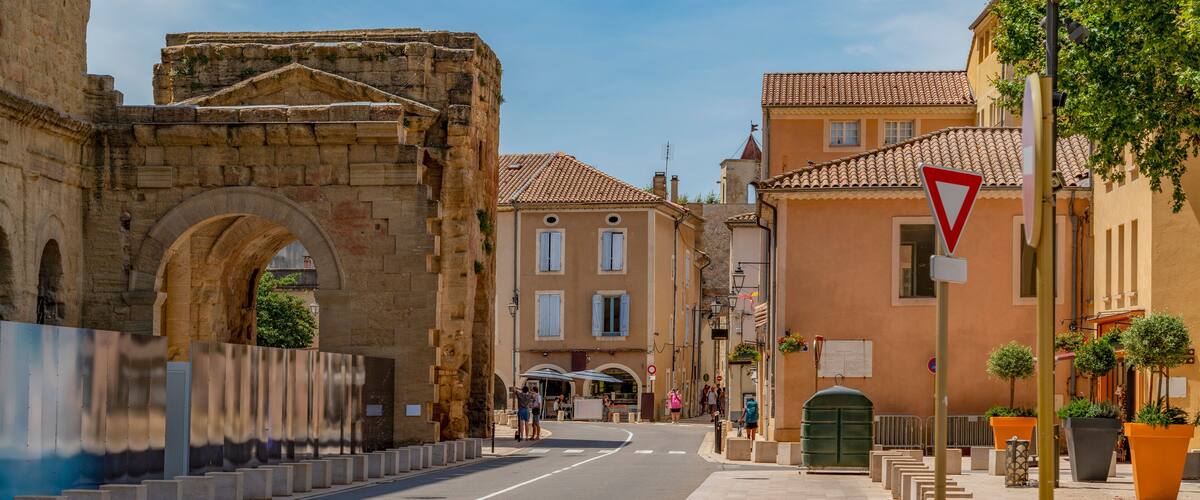 A street with a stone archway, buildings, and bollards.