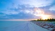 Une plage avec un ciel dégagé, des palmiers et un coucher de soleil.