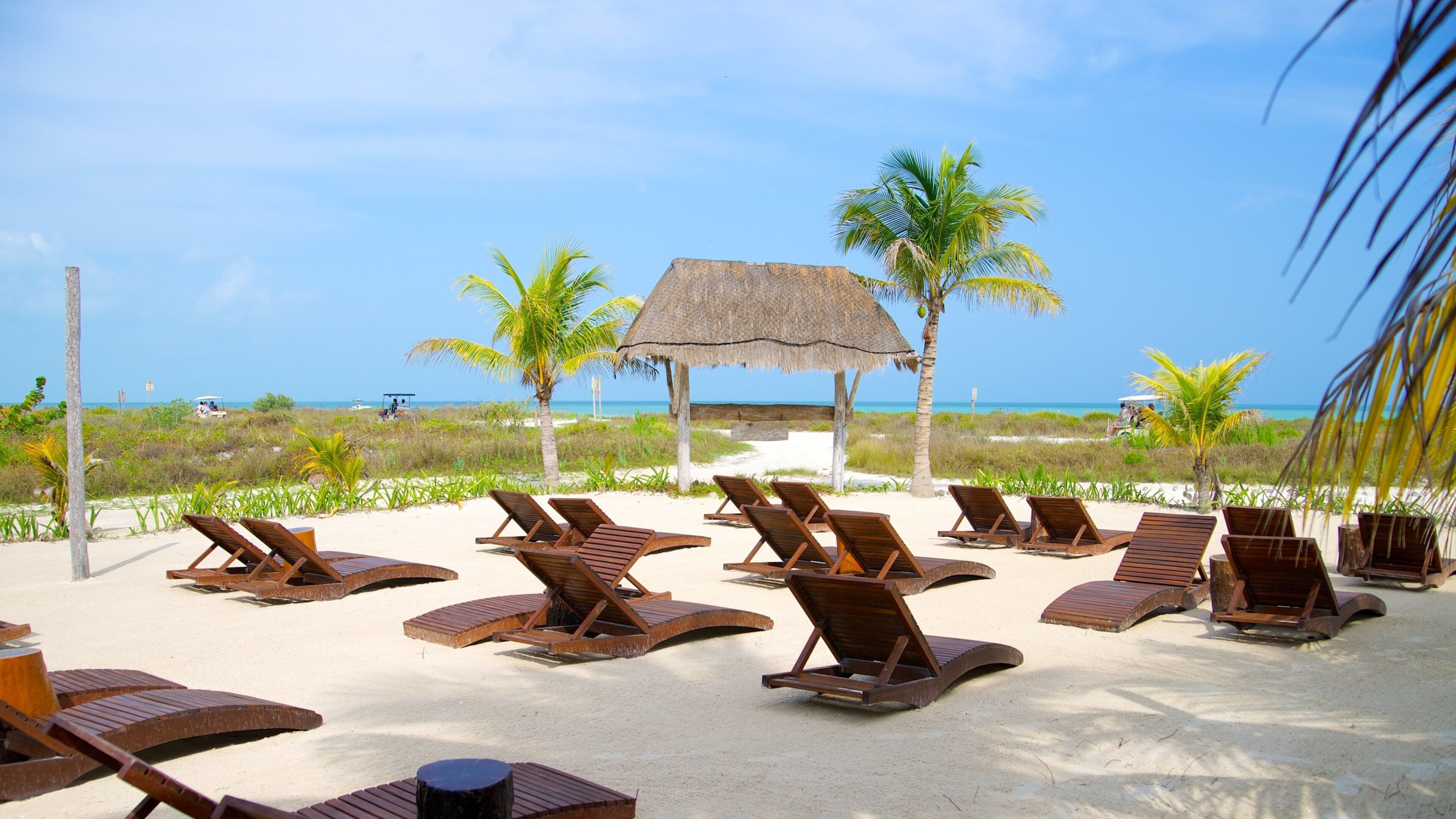 A beach with wooden lounge chairs and a thatched hut.