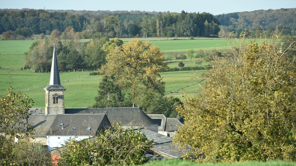 Une église dotée d’un clocher imposant, entourée de champs verdoyants et d’arbres.