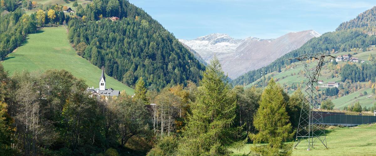 A mountainous landscape with a church, dense forests, and a power line tower.