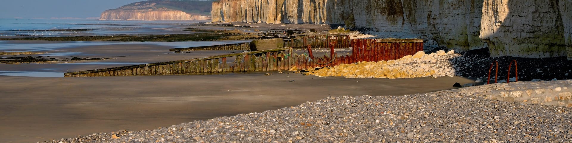 A coastal cliff with a rocky beach in the foreground and a calm sea in the background.