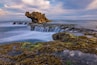 A coastal landscape with a prominent rock formation, a waterfall, and seaweed-covered rocks.