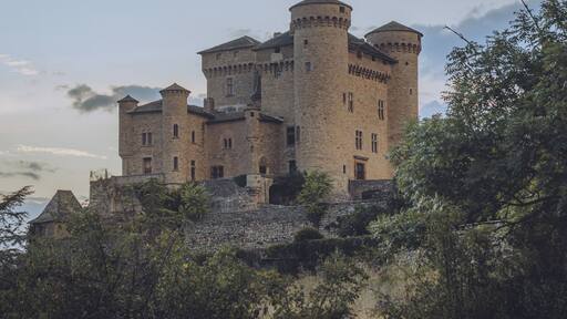 View of the ancient stone castle perched atop a hill, its towers piercing the sky against a backdrop of soft, twilight hues, Chateau de Cabrieres, Occitanie, France.
