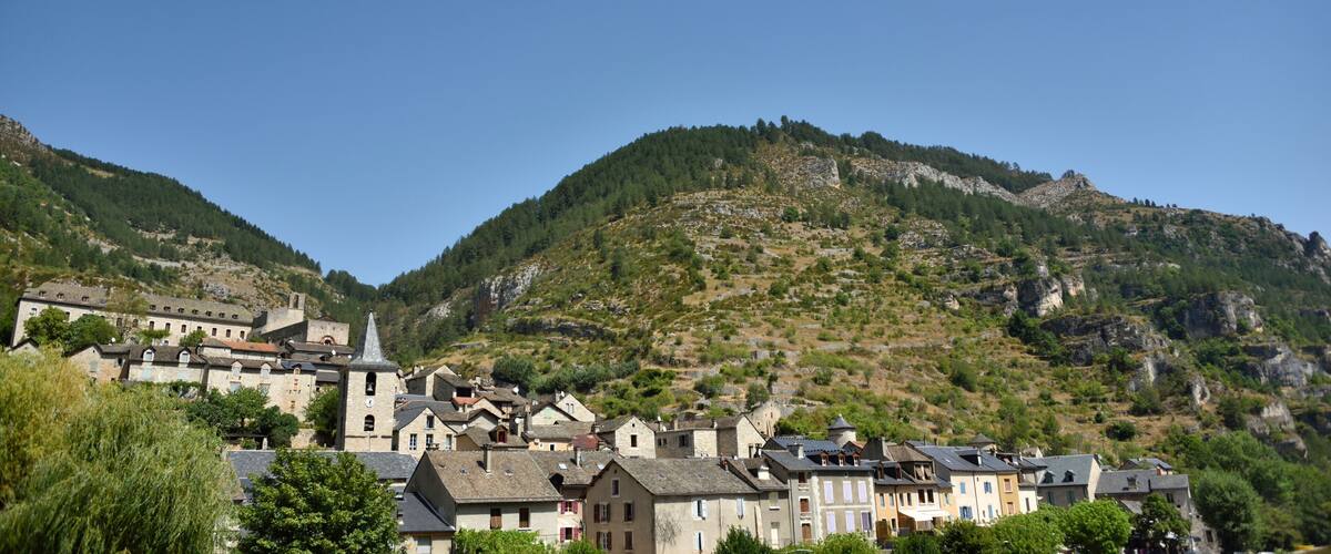 A village nestled in a valley with a prominent church and stone buildings, surrounded by forested hills.