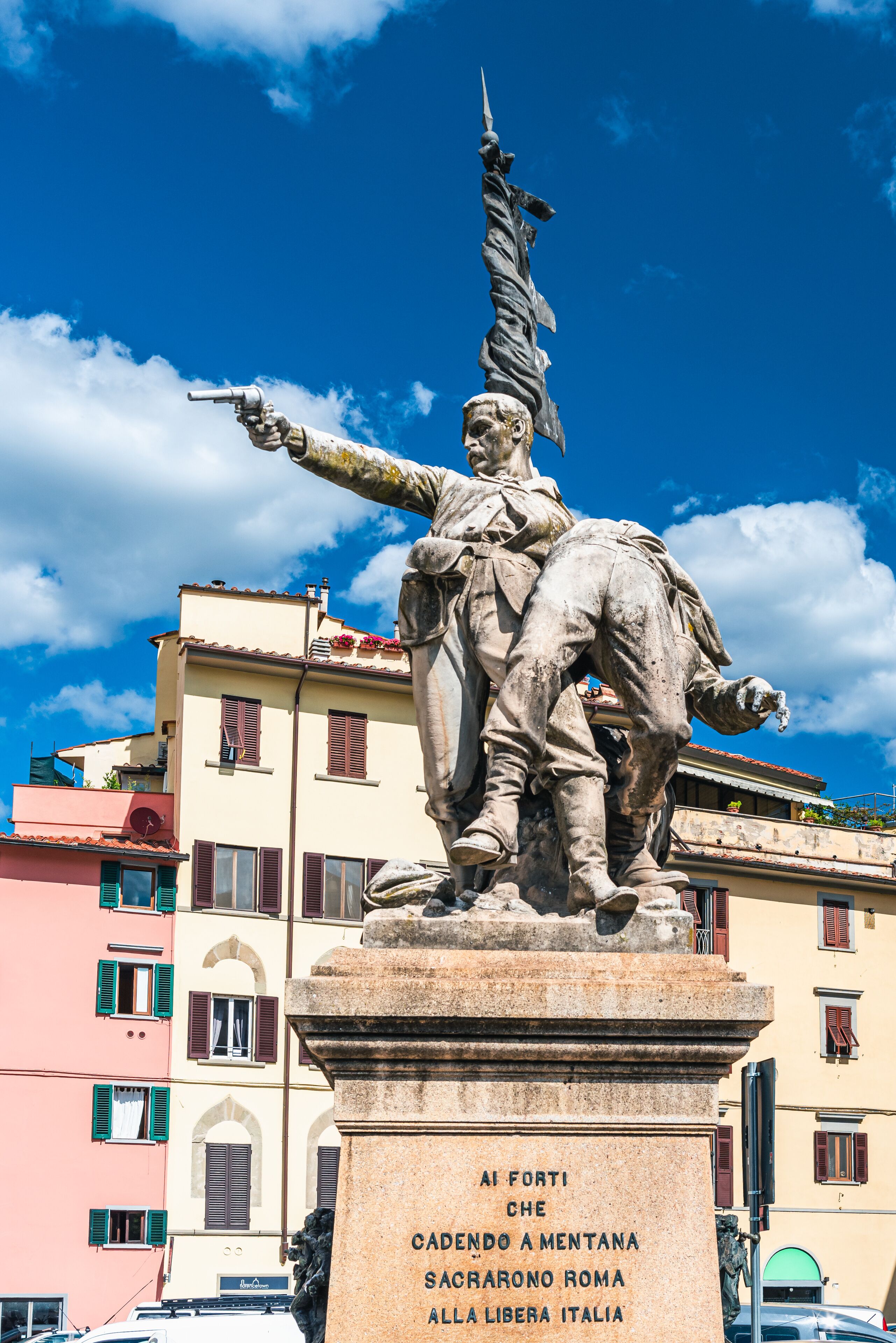A statue of a man pointing with a sword, with a plaque reading "Al Forti Che Cadendo A Mentana Sacarono Roma Alla Libera Italia".