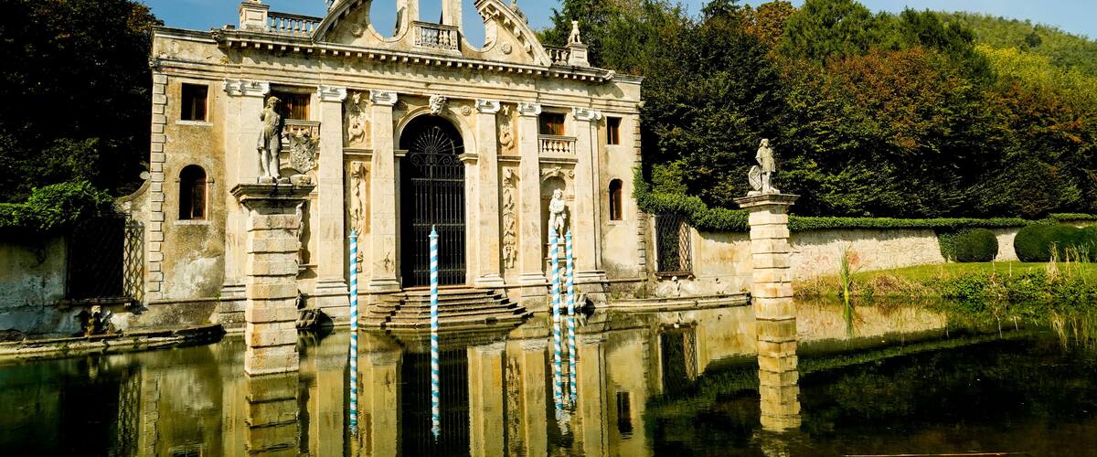 A historic building with statues and a fountain in front.