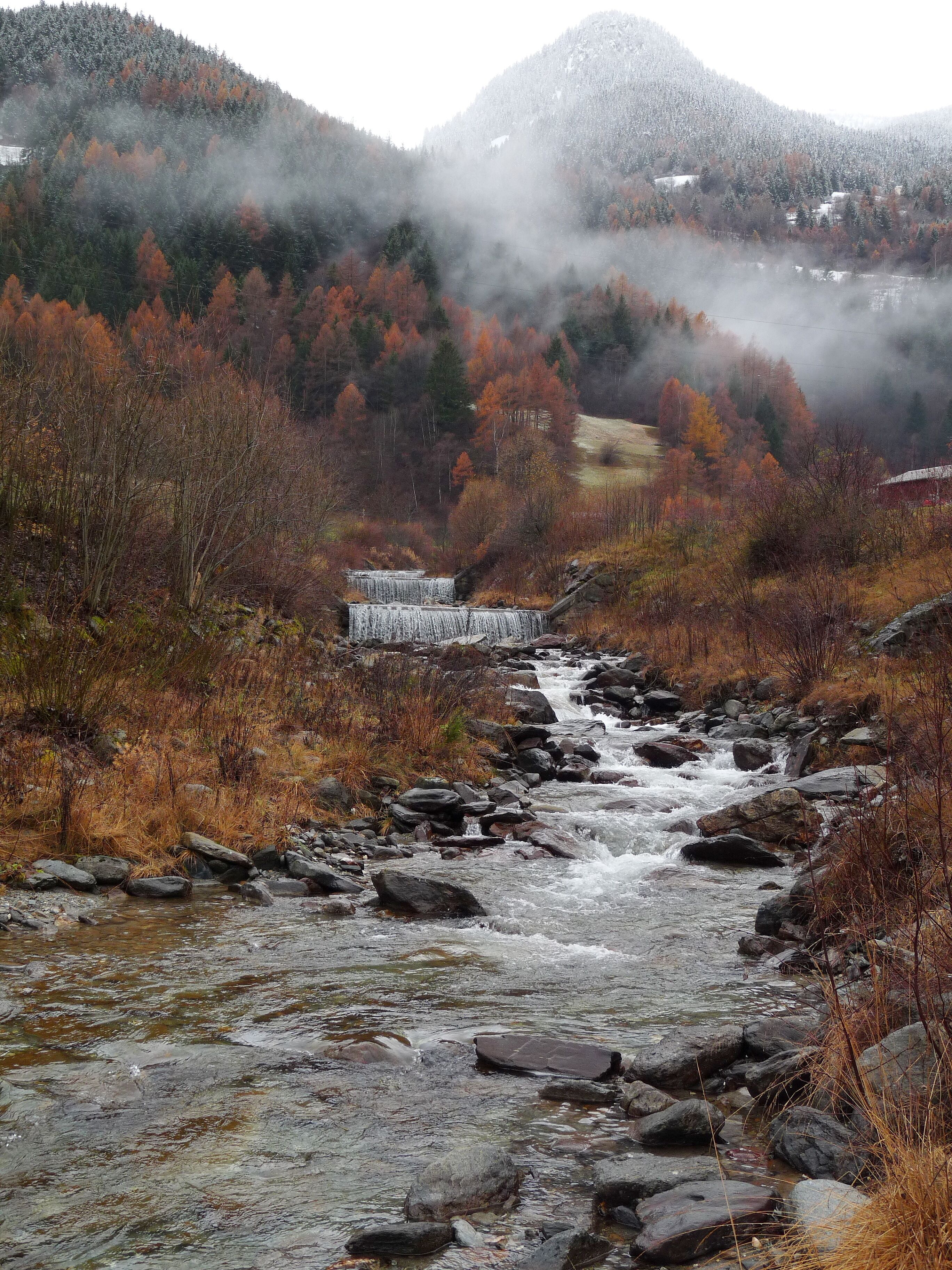 A river flowing through a mountainous area with autumn foliage and a waterfall.