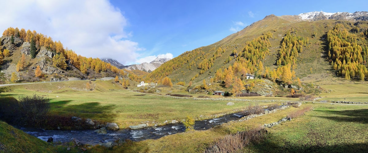 A mountainous landscape with a river, autumn-colored trees, and a small house.