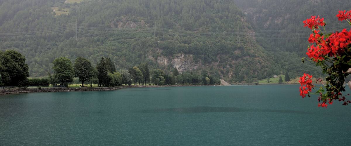 A lake surrounded by forested mountains with a small house on a hill.