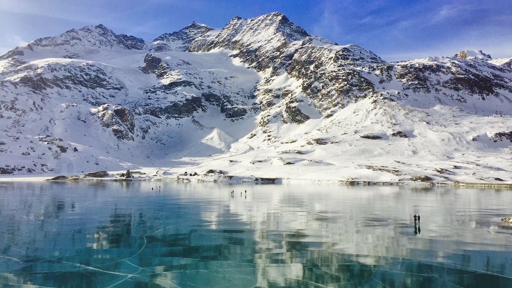 A frozen lake with reflections of snow-covered mountains under a clear sky.