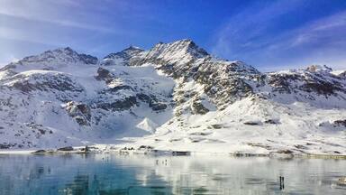 Un lago helado con reflejos de montañas nevadas bajo un cielo despejado.