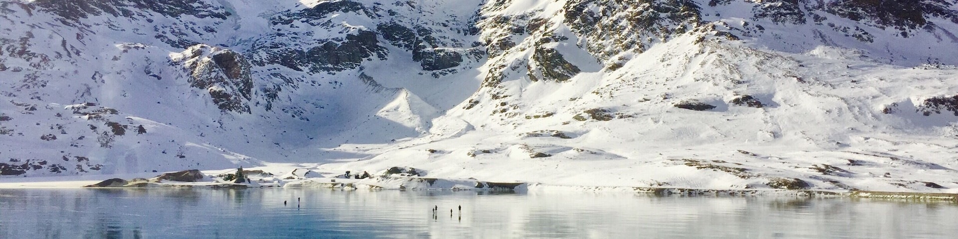 Un lago helado con reflejos de montañas nevadas bajo un cielo despejado.