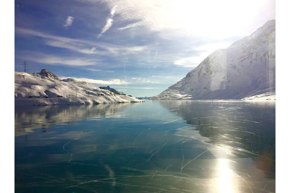 A frozen river with snow-covered banks and a mountainous backdrop.