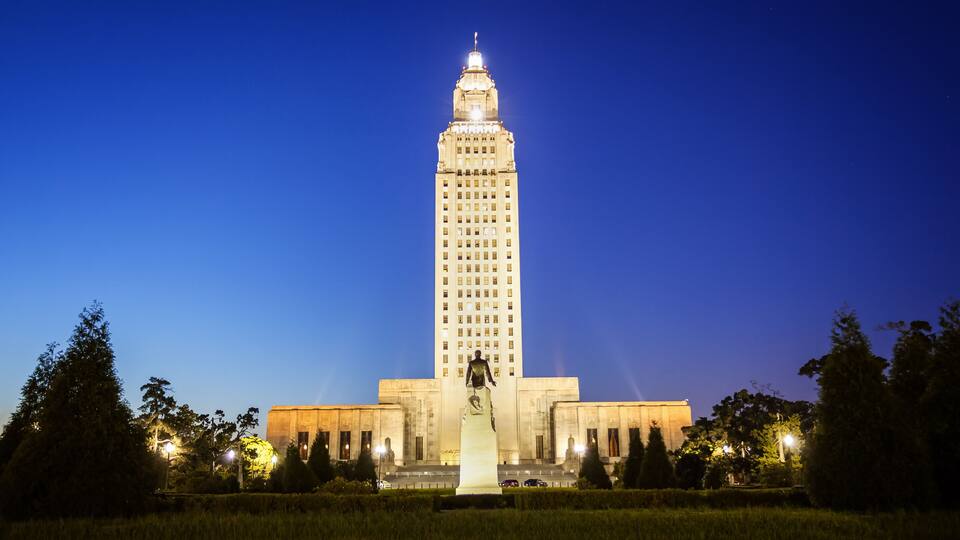 A tall, illuminated building with a statue in front, surrounded by trees and streetlights.