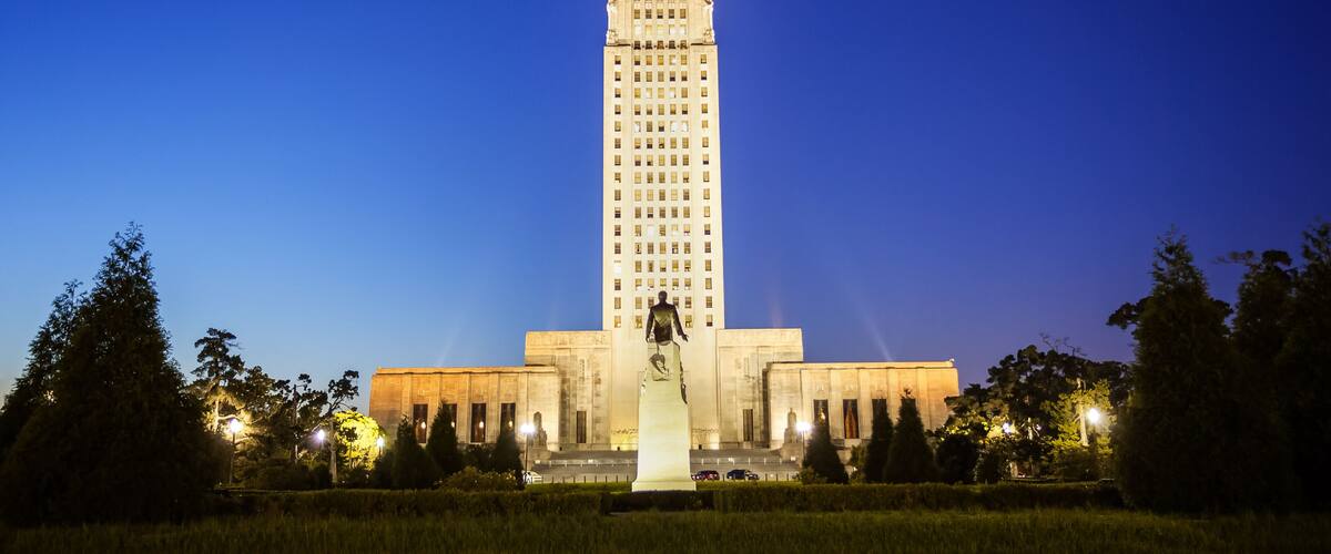 A tall, illuminated building with a statue in front, surrounded by trees and streetlights.