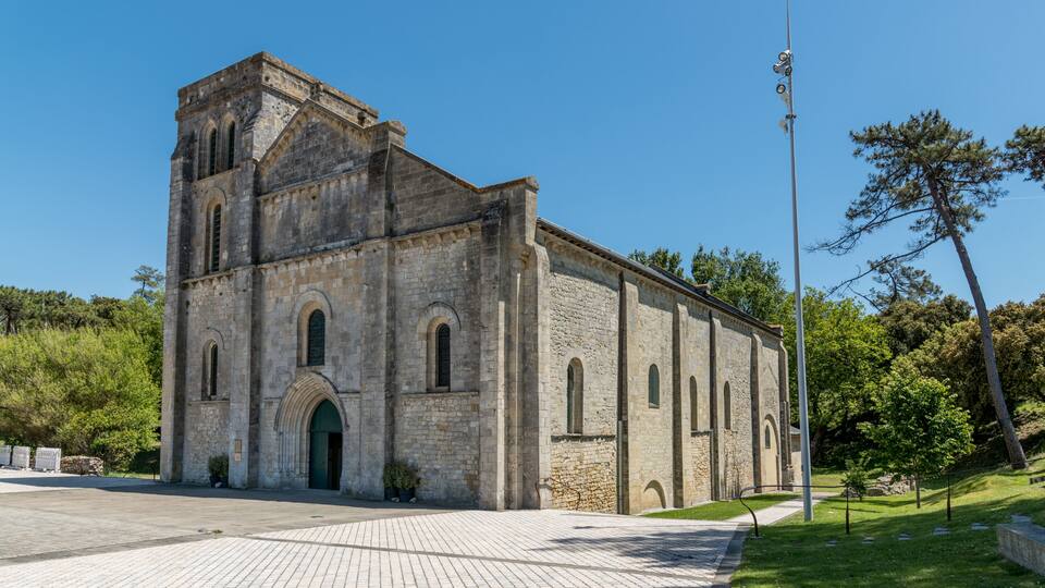 A historic stone church with arched windows and a bell tower, surrounded by a paved courtyard and greenery.