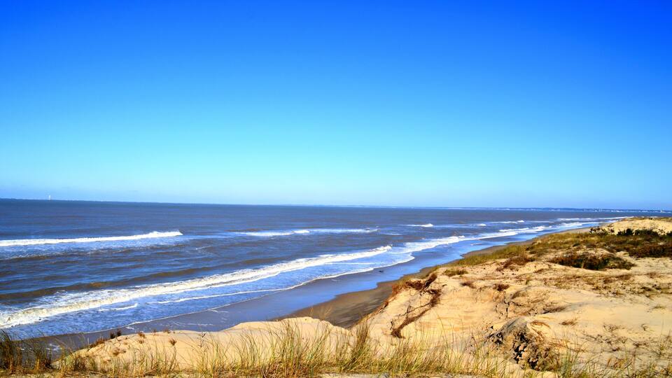 A beach with sand dunes and waves.