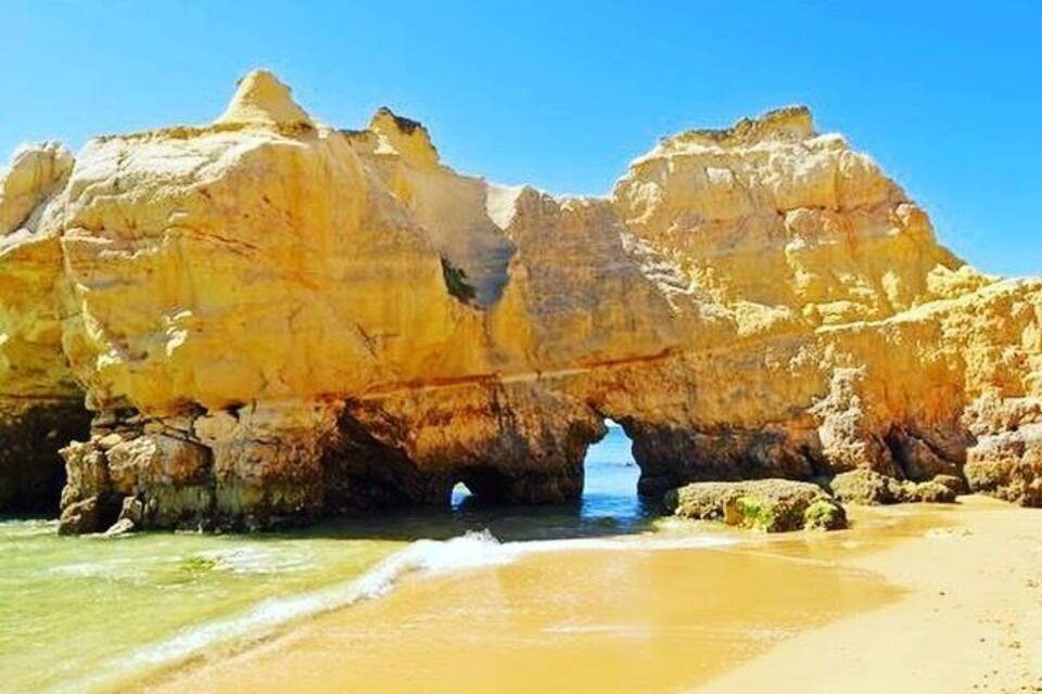 A coastal landscape with a prominent rock formation and a natural arch over the water.