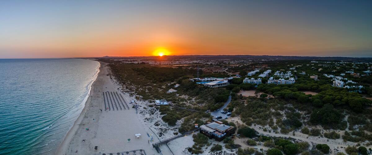 A coastal landscape with a beach, a sunset, and residential buildings.