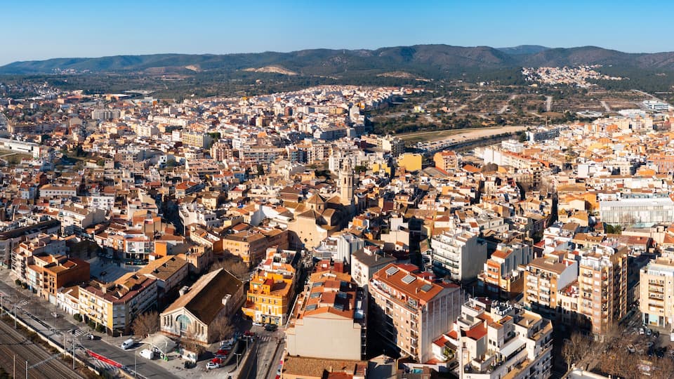 A densely packed urban area with a mix of historical and modern architecture, a prominent train station, and a mountainous backdrop.