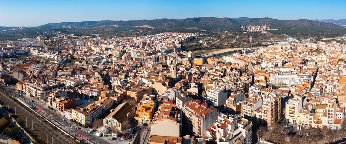 A densely packed urban area with a mix of historical and modern architecture, a prominent train station, and a mountainous backdrop.