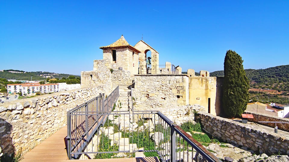 A stone fortress with a bell tower, a staircase leading up to it, and a view of the surrounding landscape.