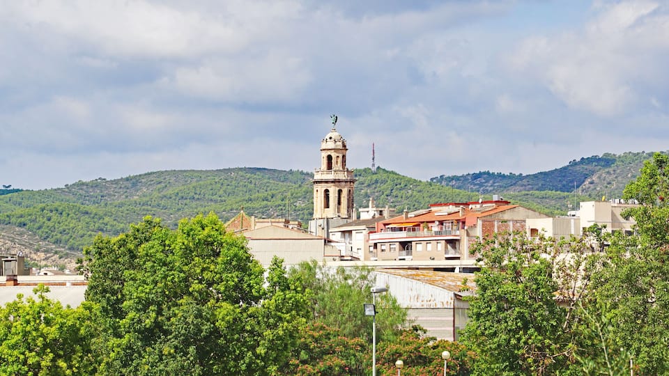 A bell tower, a church, and a hill with trees.