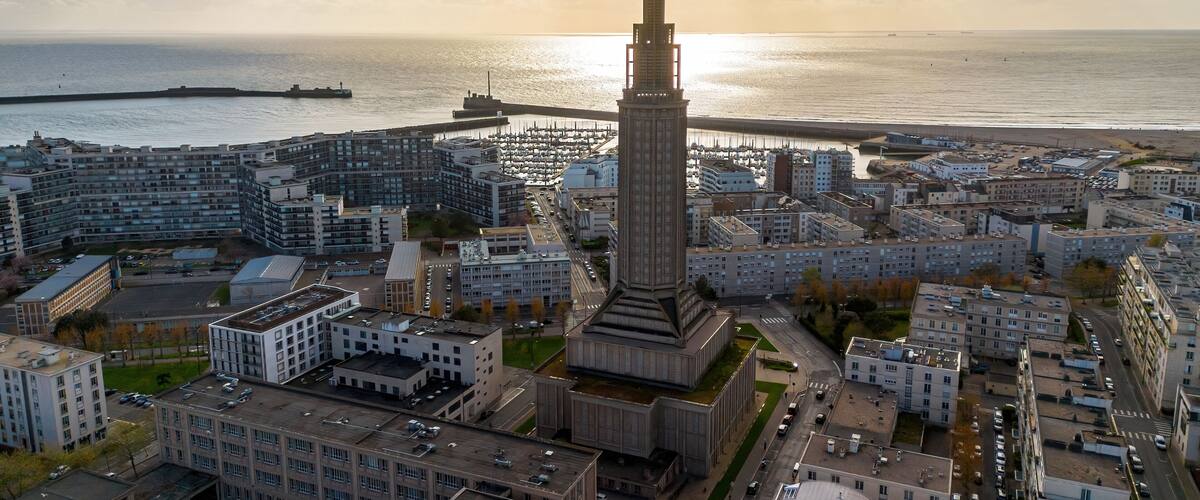 A coastal cityscape with a prominent tower, modern buildings, and a marina.