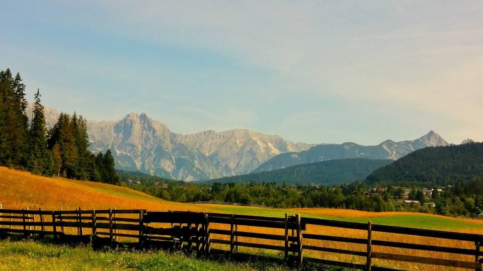 A wooden fence, a field, and a mountain range.
