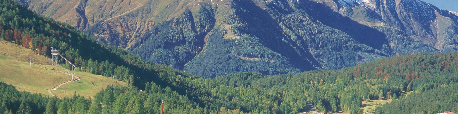 A mountain range with snow-capped peaks, a village with traditional houses, and a church with a red spire.
