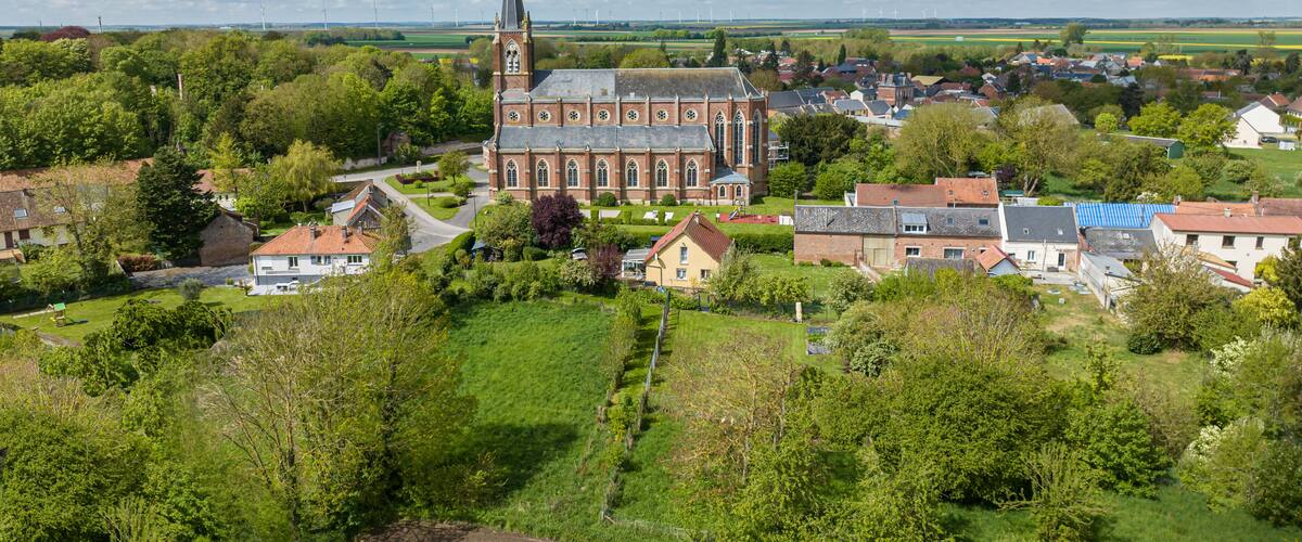 A church with a tall spire, surrounded by houses and fields.