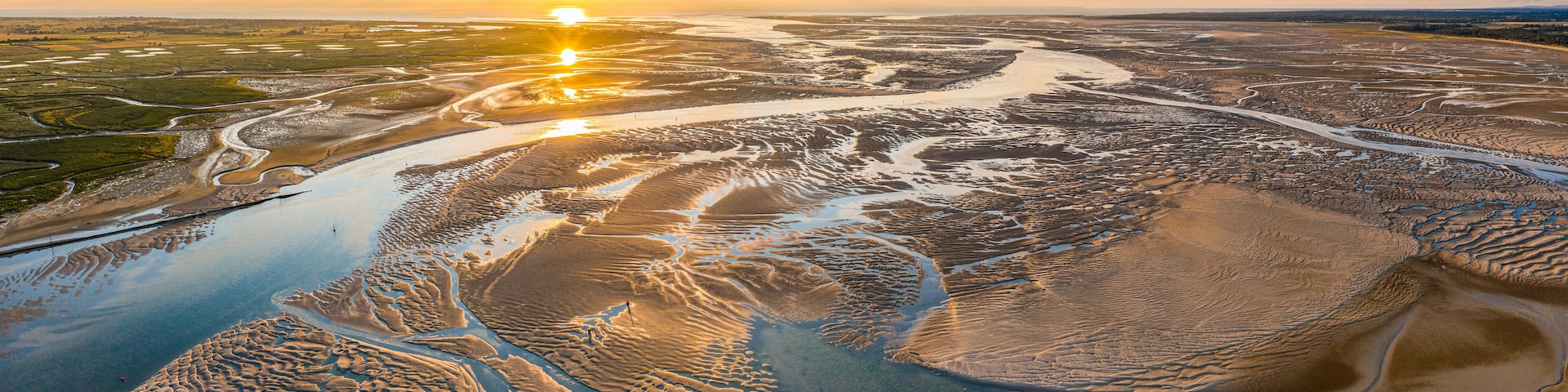 Una extensa zona de humedal con intrincados canales de agua y un atardecer de fondo.