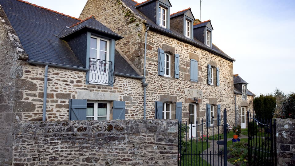 A stone house with blue shutters and a black iron gate.