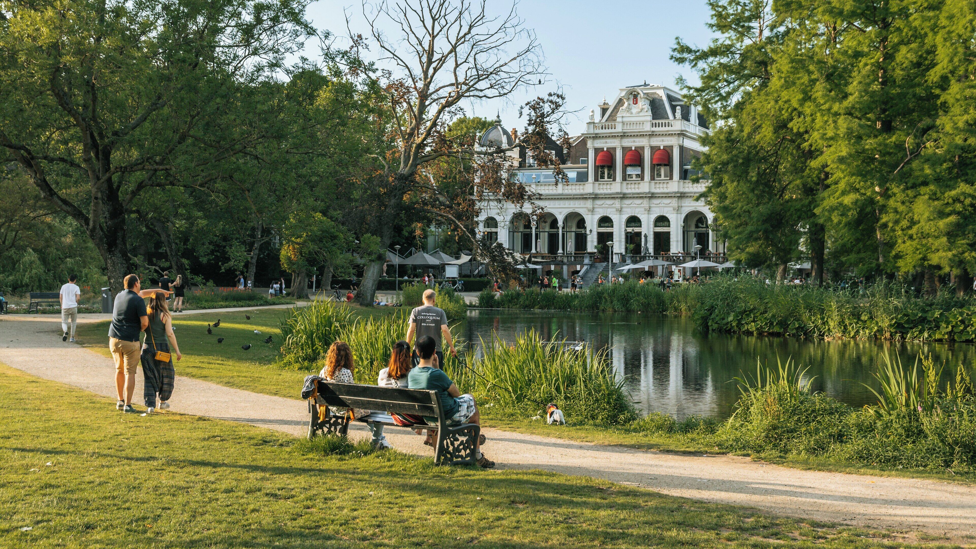 Visitors enjoy a leisurely afternoon by the pond in Vondelpark, near the Museum Quarter in Amsterdam, North Holland, Netherlands during warm weather